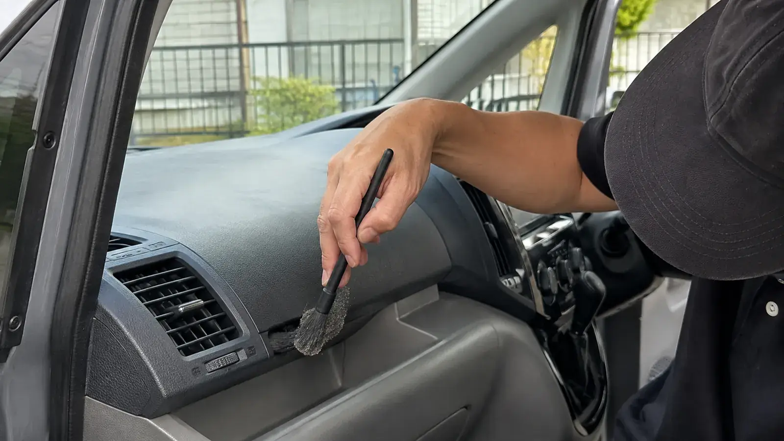 開けた運転席側のドアから手を伸ばし、エアコン吹出口の脇とダッシュボードの継ぎ目に溜まったホコリを、細いディテールブラシで掻き出しているところ